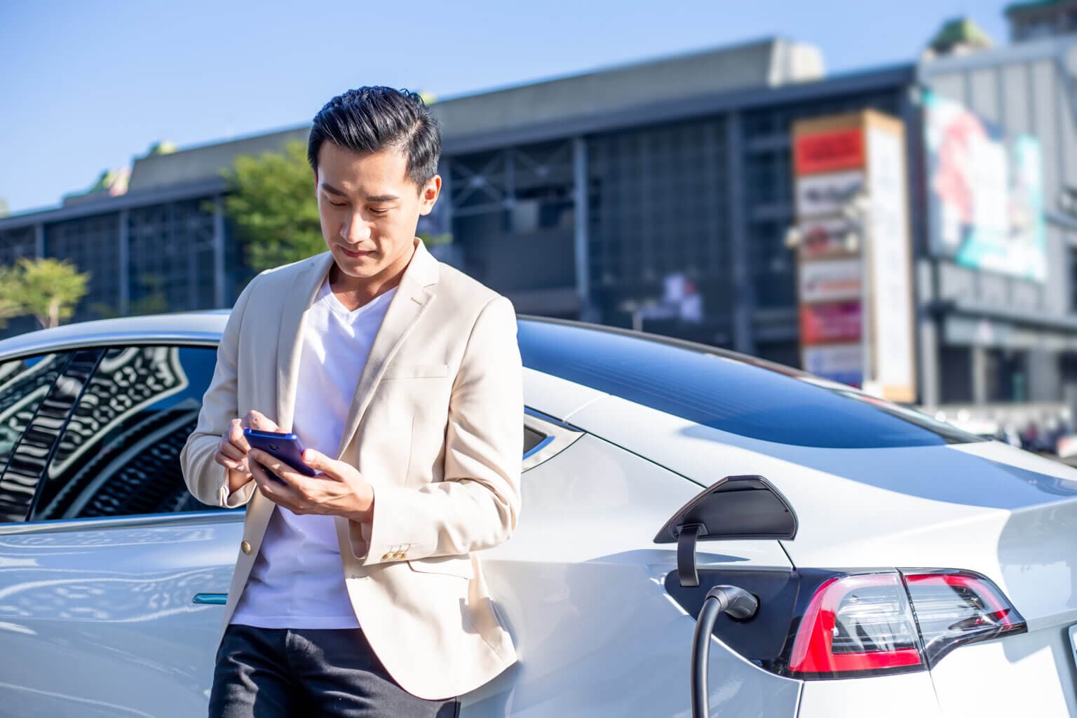 A man leaning against an electric vehicle that is charging