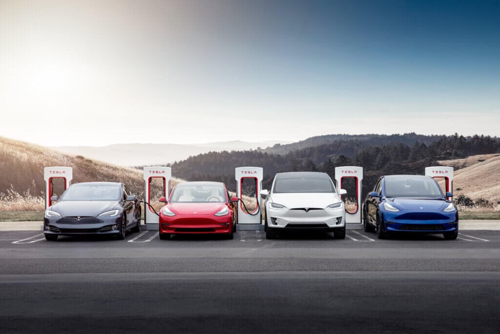 A row of colourful tesla's charging at tesla supercharger stations